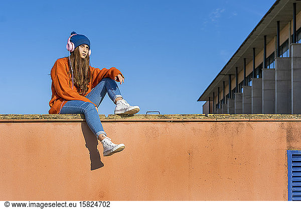 Teenage girl sitting on wall listening music with headphones
