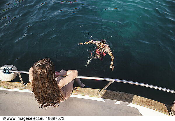 Teenage girl sitting on yacht with man swimming in sea at vacation