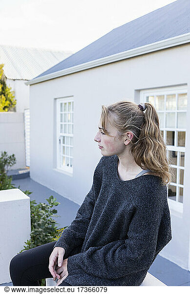 Teenage girl sitting outside a house on a low wall  waiting