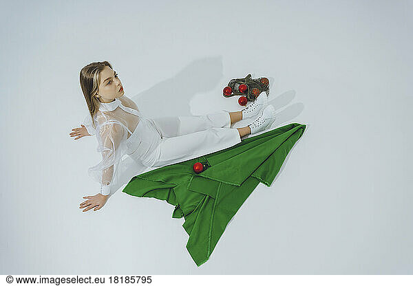 Teenage girl sitting with abstract Christmas tree and baubles over white background