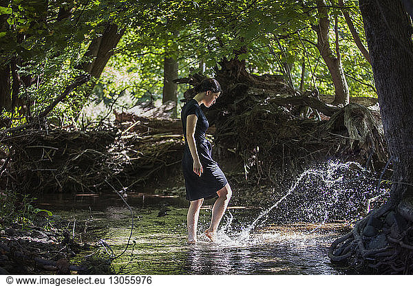 Teenage girl splashing water while standing in stream at forest