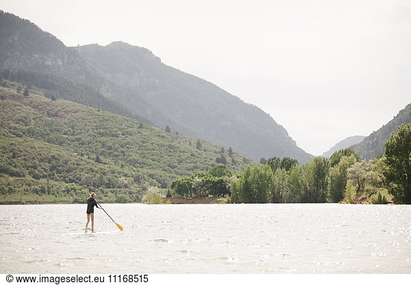 Teenage girl stand up paddle surfing on a lake.