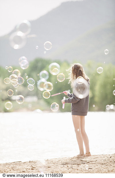 Teenage girl standing by a lake  surrounded by soap bubbles.