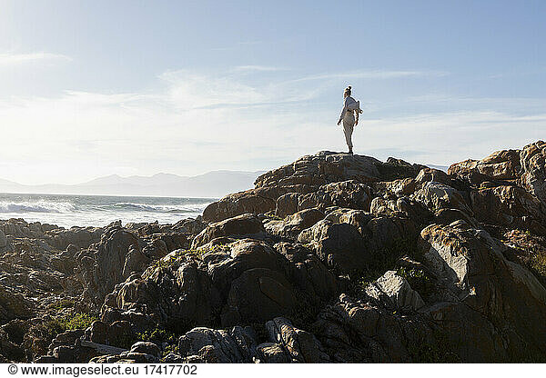 Teenage girl standing on rocky coastline  looking out to sea.