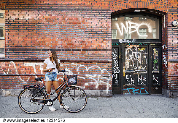 Teenage girl (14-15) standing on sidewalk with bicycle