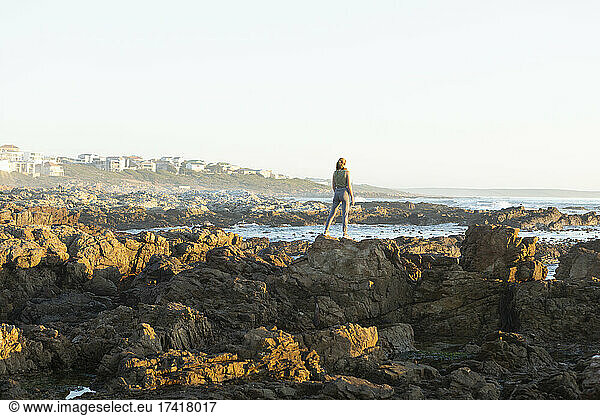 Teenage girl standing on the jagged rocks on the coastline at De Kelders.