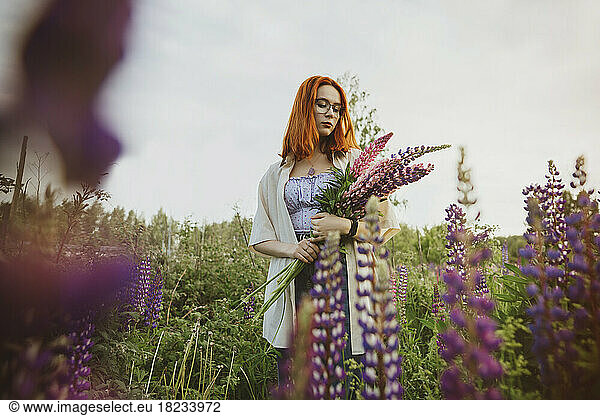 Teenage girl standing with lupin flowers under sky