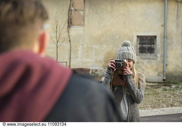 Teenage girl taking picture of her boyfriend with retro styled camera