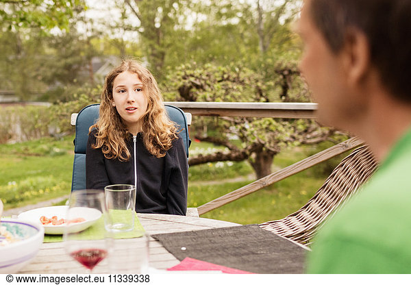 Teenage girl talking to father at table in yard