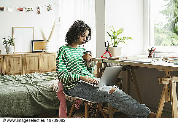 Teenage girl using laptop and drinking hot chocolate at home
