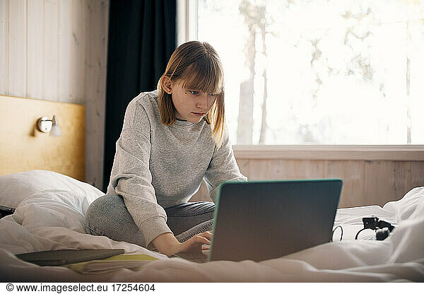 Teenage girl using laptop while doing homework in bedroom
