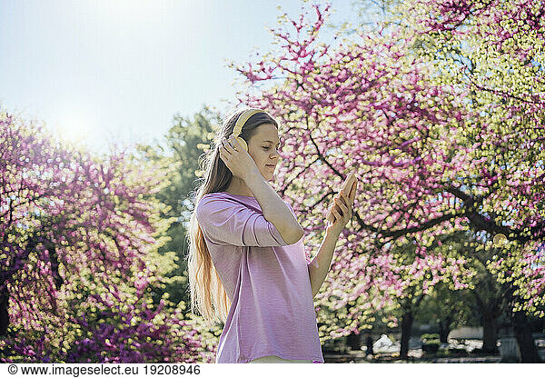 Teenage girl using smart phone and enjoying music with headphones at park