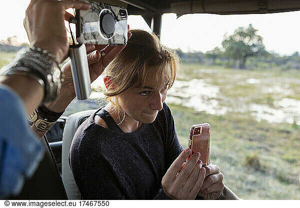 Teenage girl using smart phone to take a picture during a safari jeep drive.