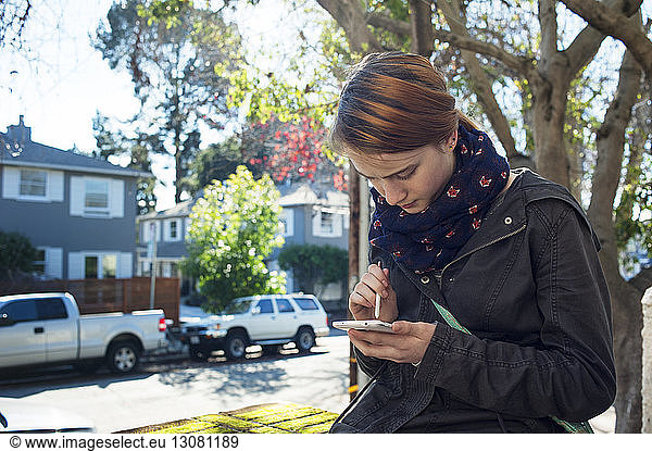 Teenage girl using smart phone with stylus in city