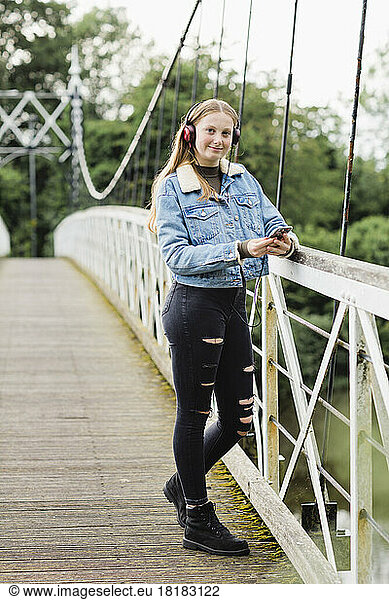 Teenage girl using smartphone and listening music on a bridge