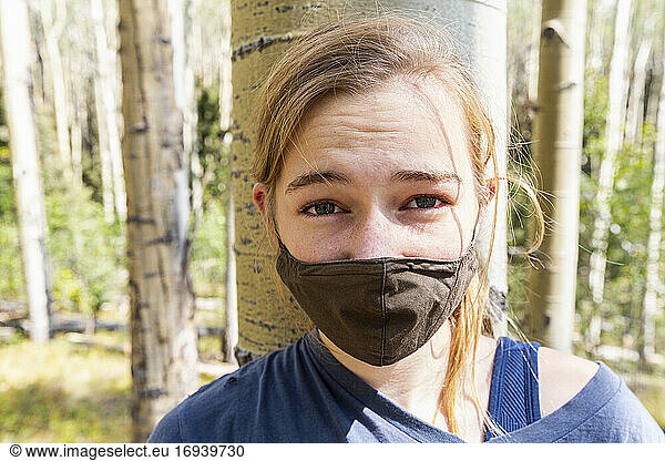 Teenage girl wearing COVID-19 mask in forest of Aspen trees