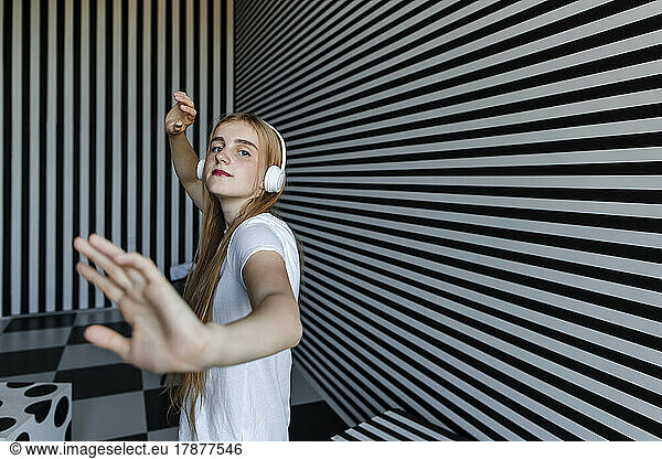 Teenage girl wearing headphones dancing by striped wall