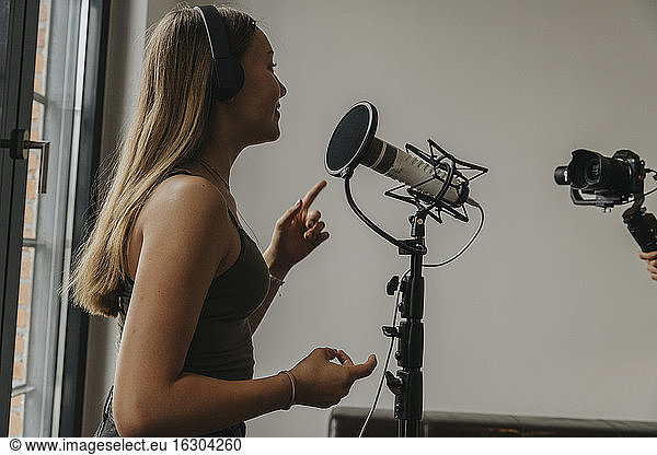 Teenage girl wearing headphones singing over microphone in studio