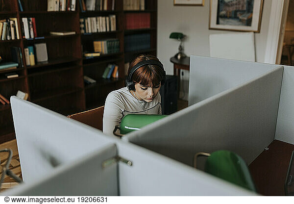 Teenage girl wearing wireless headphones while sitting in library