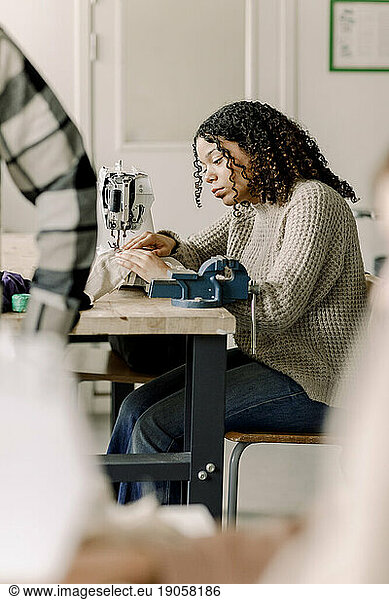 Teenage girl with curly hair using sewing machine in art class at high school