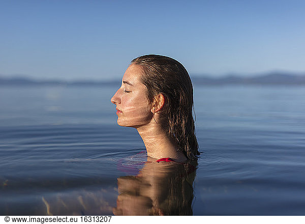 Teenage girl with eyes closed  head and shoulders above the calm waters of a lake at dawn