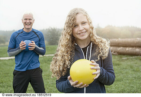 Teenage Girl with her father exercising with yoga ball on the field and smiling during dawn  Bavaria  Germany