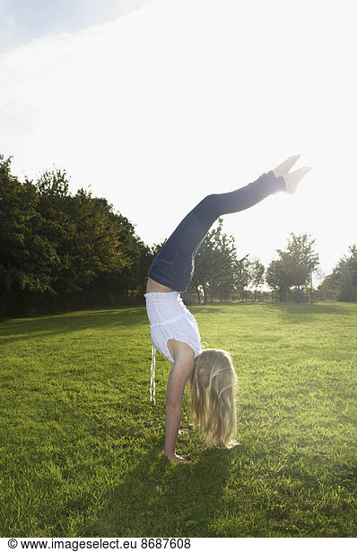 Teenage girl with long blond hair doing a headstand.