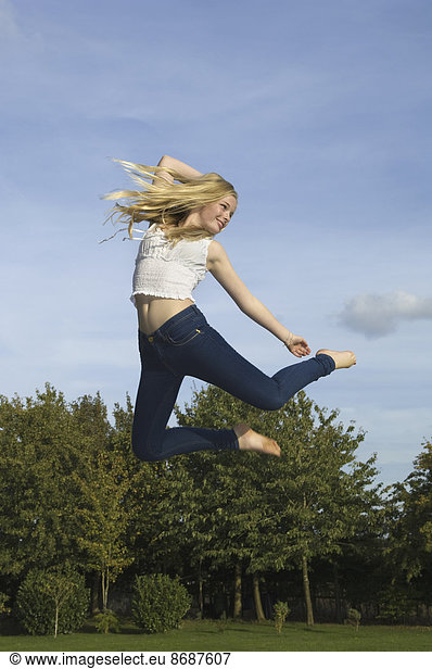 Teenage girl with long blond hair jumping in the air.