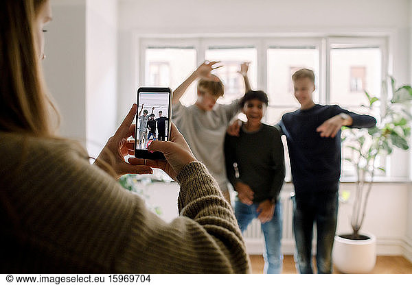 Teenage girl with mobile phone filming male friends dancing in living room