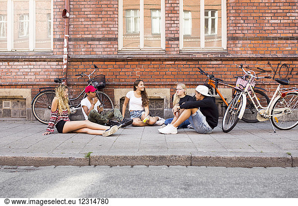 Teenage girls and teenage boys (14-15) sitting on sidewalk