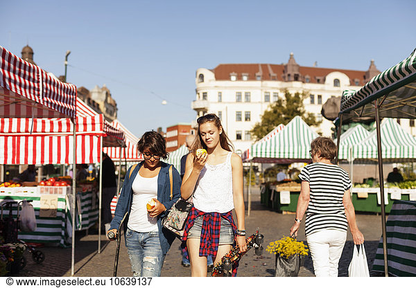 Teenage girls holding apple and walking in market