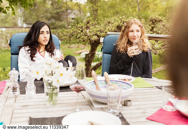 Teenage girls looking away while sitting at outdoor table in yard