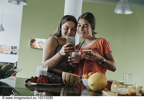 Teenage girls preparing fresh fruit smoothies  sharing smartphone pictures