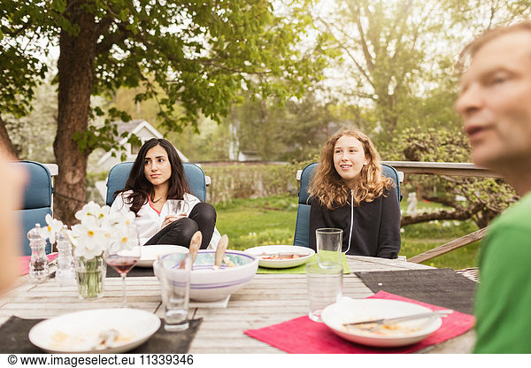 Teenage girls sitting with father at table in yard