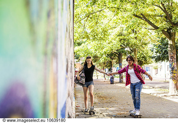 Teenage girls skateboarding at footpath by wall