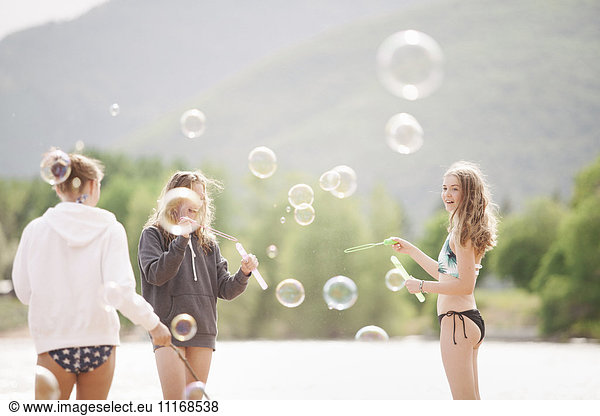 Teenage girls standing by a lake  surrounded by soap bubbles.