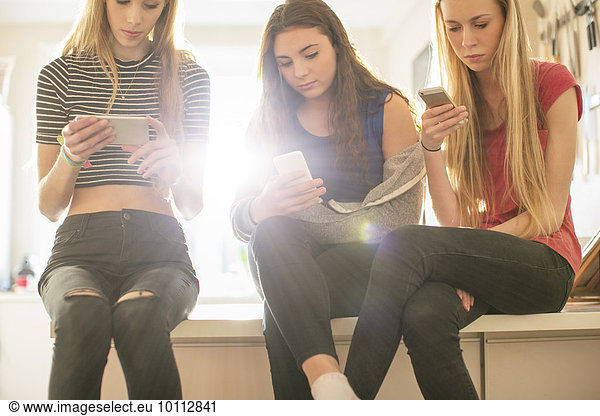 Teenage girls texting with cell phones in kitchen