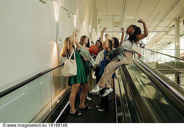 Teenage girls with hand raised enjoying on escalator in mall