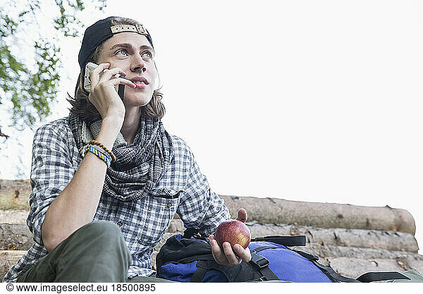 Teenage male hiker talking on mobile phone and holding an apple  Bavaria  Germany