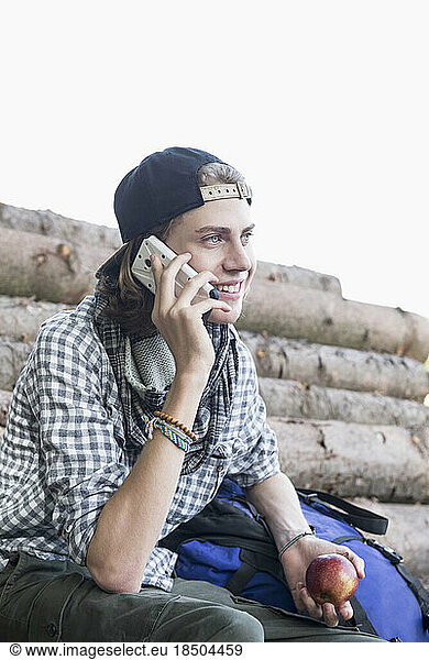 Teenage male hiker talking on mobile phone and holding an apple  Bavaria  Germany