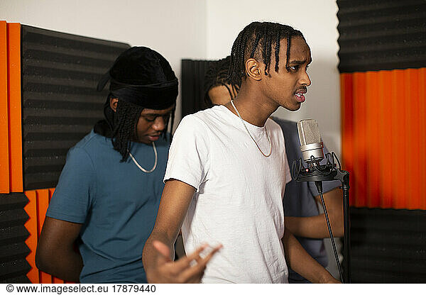 Teenage rapper with friends recording song on microphone in studio