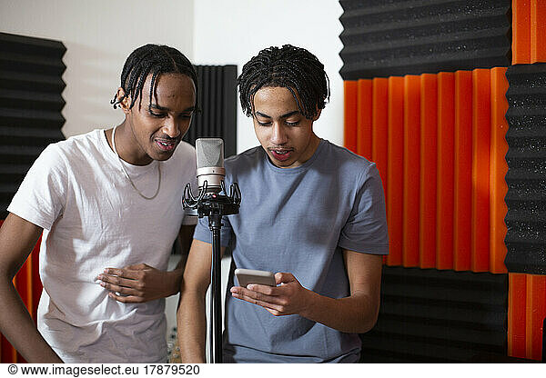 Teenage rappers sharing smart phone while recording song in studio