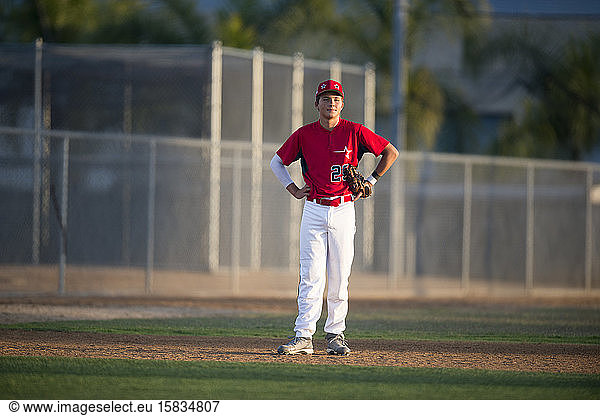 Teenager-Baseballspieler in roter Uniform steht auf dem Innenfeld