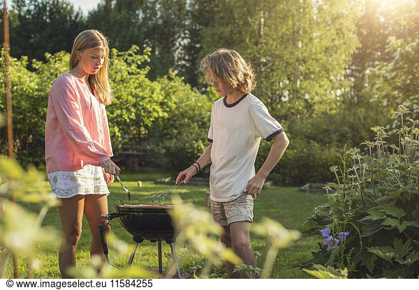 Teenager-Geschwister beim Grillen im Garten an sonnigen Tagen