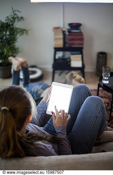 Teenager girl using digital tablet while sitting on sofa at home