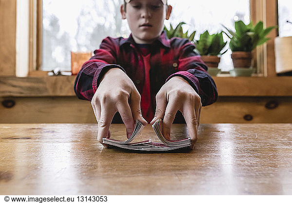 Teenager Junge mischt Karten auf Holztisch in Hütte