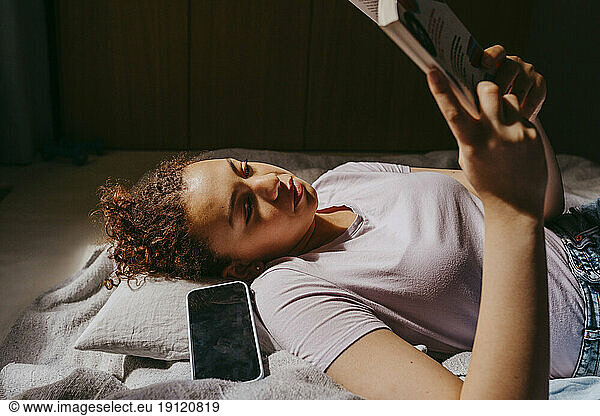 Teenager-Mädchen  das auf dem Bett liegend ein Buch liest