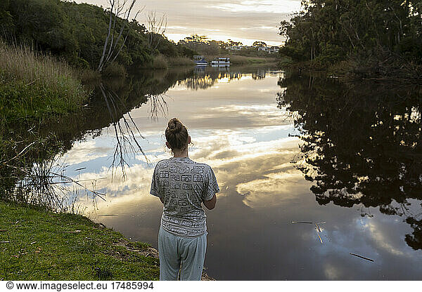 Teenager-Mädchen  das in der Abenddämmerung an einem Fluss steht.