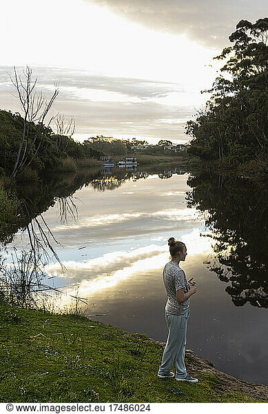 Teenager-Mädchen  das in der Abenddämmerung an einem Fluss steht.