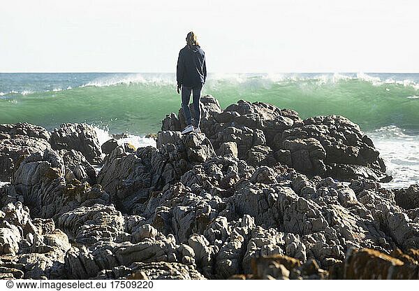 Teenager-Mädchen klettert auf den zerklüfteten Felsen an einem Strand  große Wellen brechen am Ufer